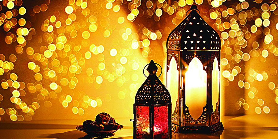 Ornamental Arabic lanterns with burning candles. Glittering golden bokeh lights. Plate with date fruit on the table. Greeting card for Muslim holiday Ramadan Kareem. Iftar dinner background.